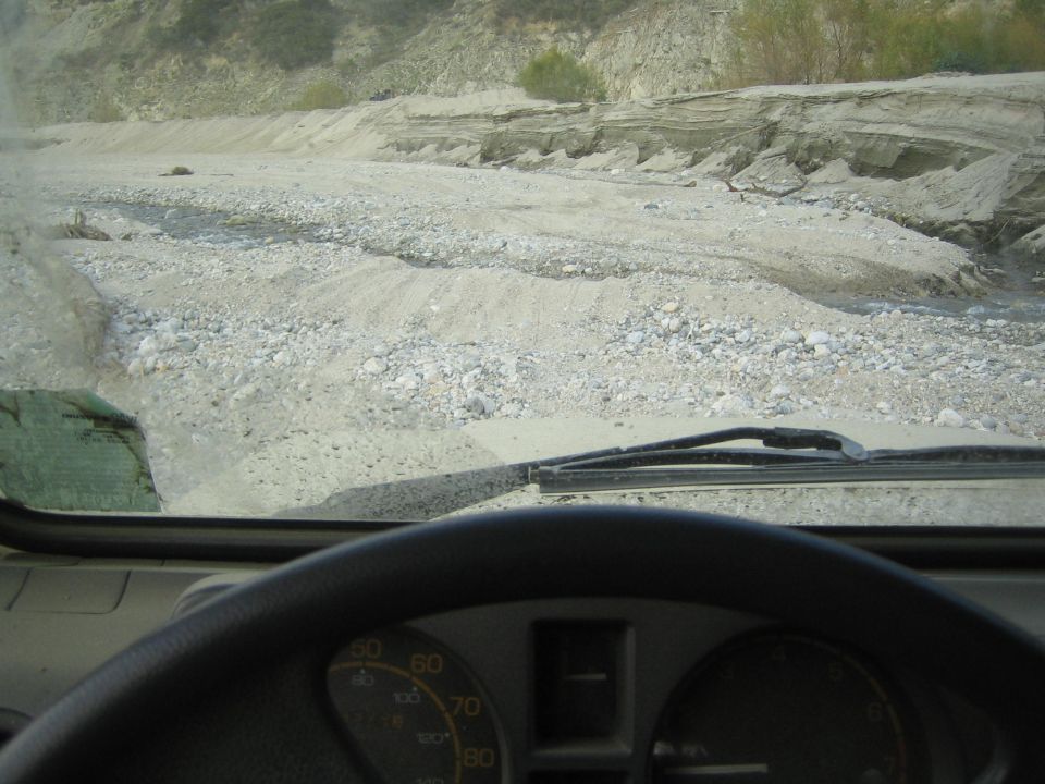 view from inside a vehicle driving on a rough, rocky, and sandy path with hills in the background