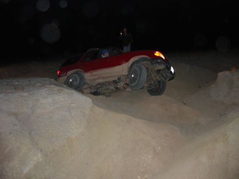 1997 Ford Ranger - Night rock-crawling shot of a red and tan two-tone SUV tipped at a steep angle on an eroded rock ledge with its left front wheel lifted off…