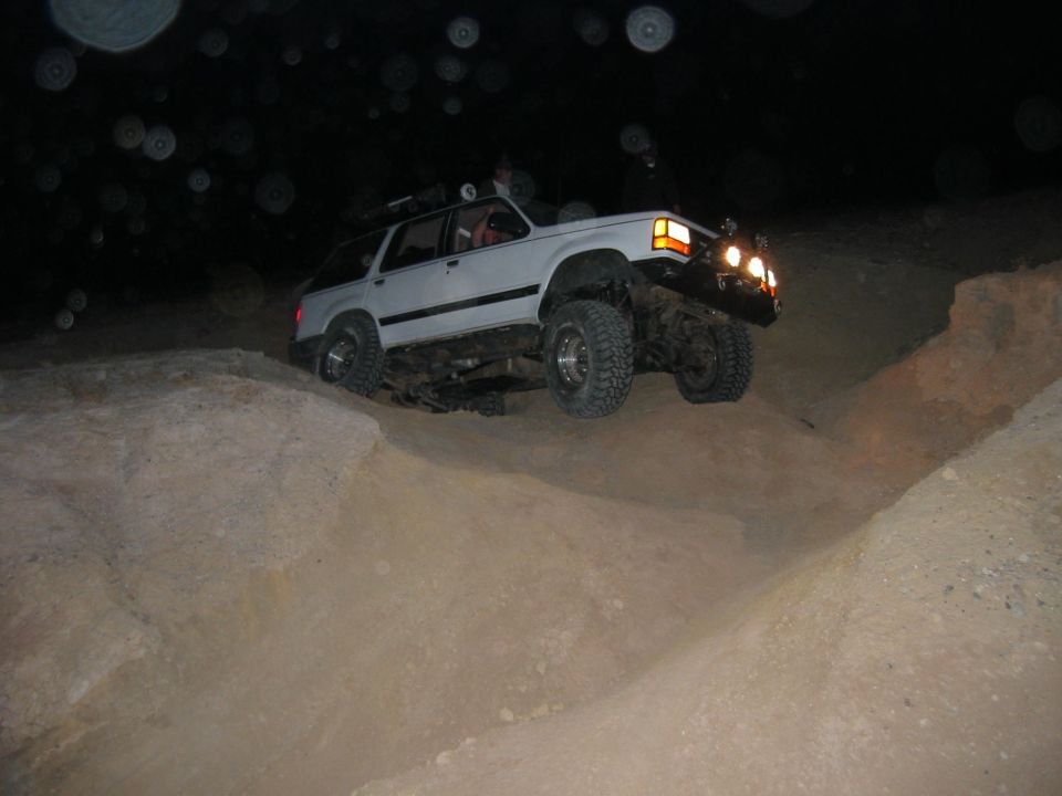 White 1997 Ford Ranger SUV with off-road tires climbing a dirt hill at night