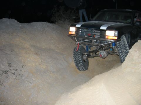 1997 Ford Ranger - Night shot of a black Chevrolet/GMC full-size pickup dropping into a sandy wash with its solid front axle fully drooped, showing a bare tub…