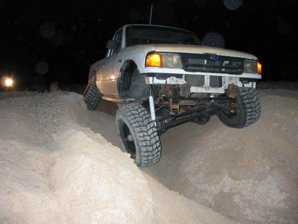 White pickup truck with lifted suspension driving on a dirt hill at night