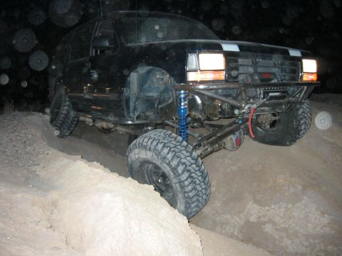 1997 Ford Ranger - Night three-quarter front shot of a black Chevrolet/GMC full-size 4x4 straddling a sandy ditch, front axle articulated with the driver-side…
