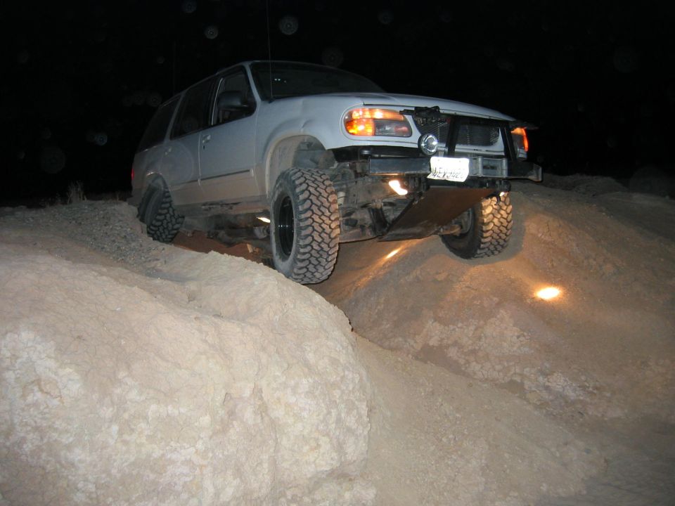 White SUV with lifted suspension and large tires driving over dirt mounds at night