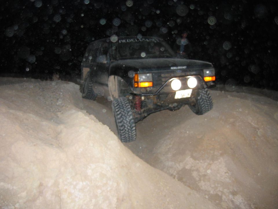 Black SUV with off-road tires driving on a dirt hill at night. Has extra lights on the front bumper