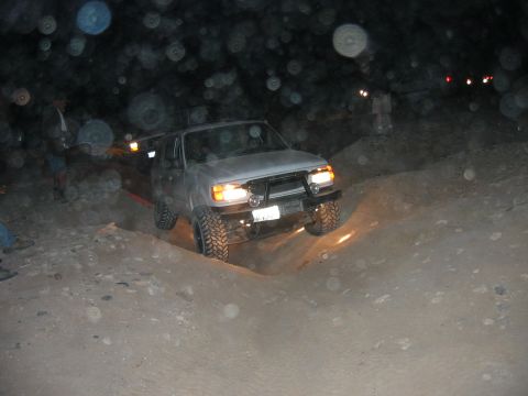 1997 Ford Ranger - Night shot of a lifted silver-gray SUV with headlights on, flexing through a rutted dirt whoop with its front wheel drooped into the hole,…