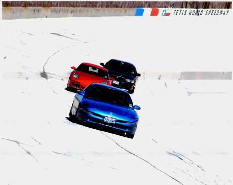 1996 Ford Probe - Three cars are on a race track with the Texas World Speedway sign in the background.