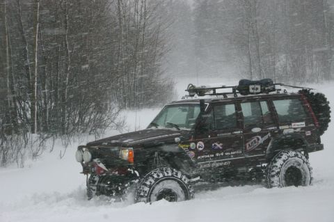 2003 Jeep TJ - A Jeep Cherokee XJ navigates a snowy landscape with trees in the background.
