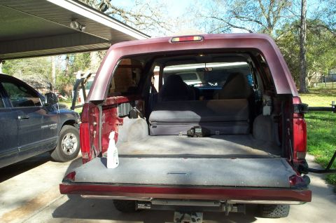 1996 Ford Bronco - The rear of a red Ford Bronco is open, revealing its cargo space and a blue pickup truck parked nearby.