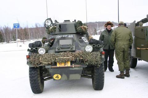 2003 Jeep TJ - A military armored car is parked in a snowy outdoor setting with two individuals observing it.