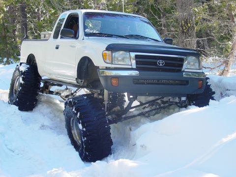 1986 Ford Bronco - This heavily modified pickup truck is shown off-road in a snowy environment.