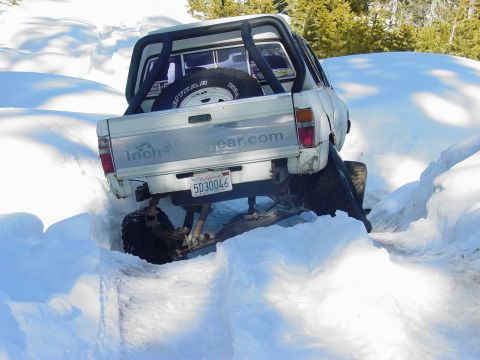 1986 Ford Bronco - A modified pickup truck navigates a snowy trail, with its rear end partially submerged in snow.