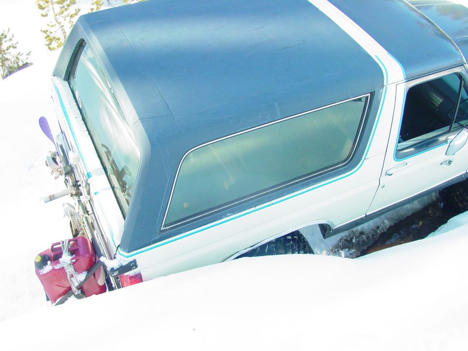 Rear view of a 1986 Ford Bronco in the snow with skis and gas cans