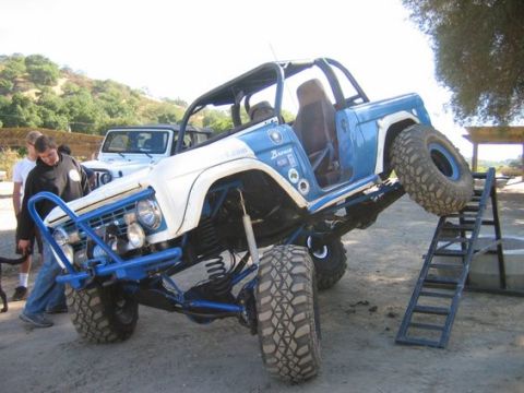 1971 Ford Bronco - A heavily modified Ford Bronco is shown with its front tire on a ramp, while another Jeep is parked behind it.