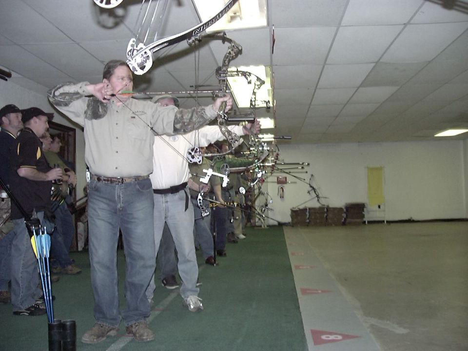 People practicing archery indoors, aiming bows at targets down a range