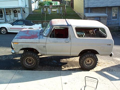 1978 Ford Bronco - This lifted Ford Bronco has a primer hood and a red roof, with a white convertible Mustang parked behind it.
