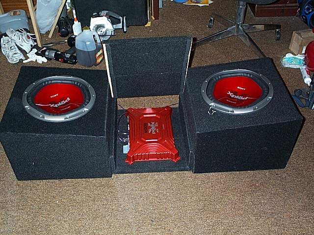 Two Sony Xplod 12-inch subwoofers in carpeted boxes flanking a red amplifier