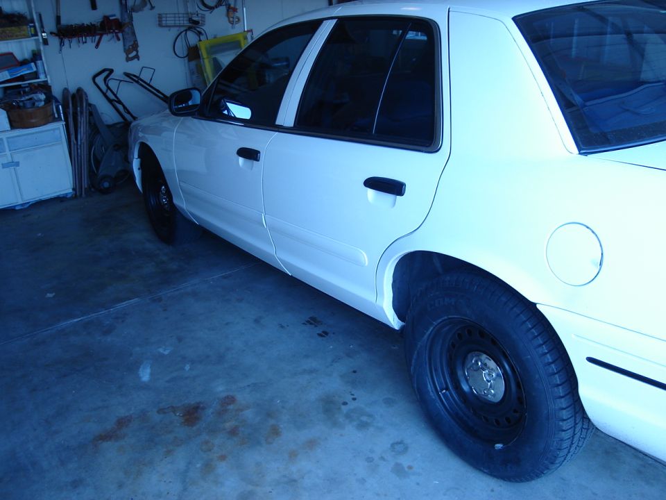 White sedan parked in a garage, side view. Black steel wheels and tinted windows are visible