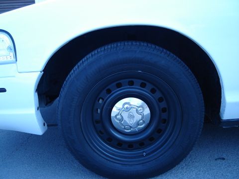 2000 Ford Crown Victoria - Close-up of a white car's front fender and wheel, a Ford badge on the hubcap.