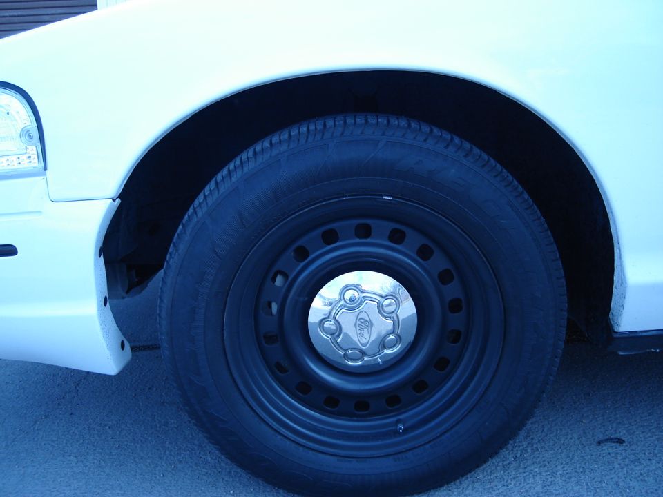 White car wheel with Ford badge on hubcap, close-up of front fender