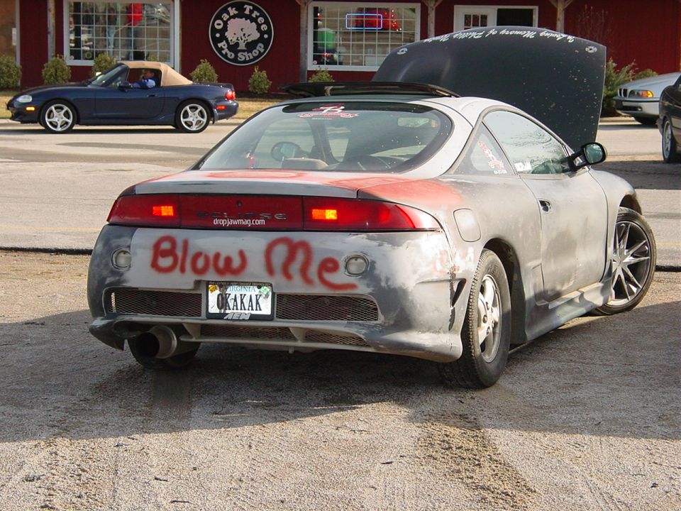 Silver Mitsubishi Eclipse coupe, rear view, 'Blow Me' painted on primer bumper, Virginia plate.