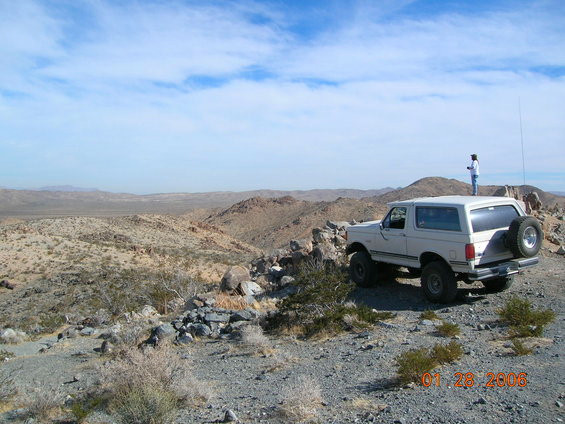 White Ford Bronco parked on a rocky hill, person standing on the roof. Date stamp 01-28-2006
