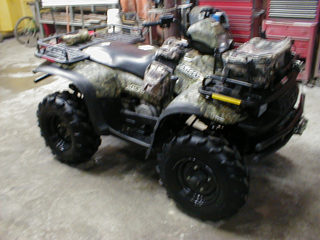 Camo-patterned Polaris four-wheeler ATV parked in a garage with knobby tires and rear storage bags.