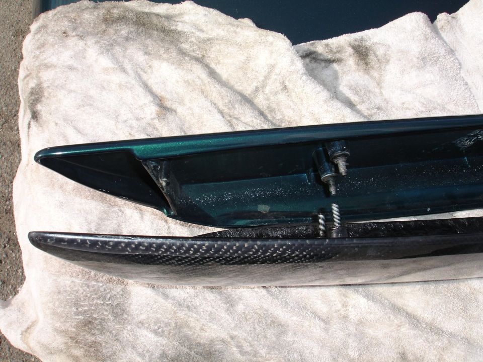 Carbon fiber spoiler next to green car part with visible bolts