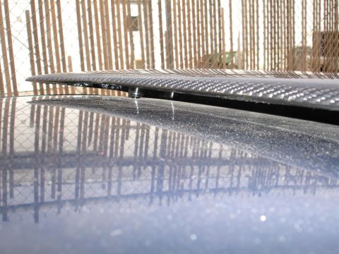 1995 Ford Taurus - A close-up view of a carbon fiber spoiler attached to the rear of a blue vehicle.