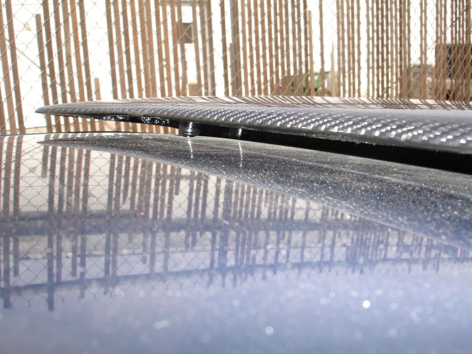 Carbon fiber spoiler mounted on a blue car's trunk, viewed from the side