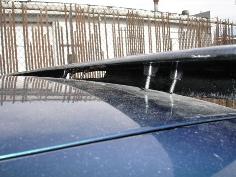 1995 Ford Taurus - Aftermarket carbon fiber spoiler attached with bolts to the trunk of a blue vehicle.