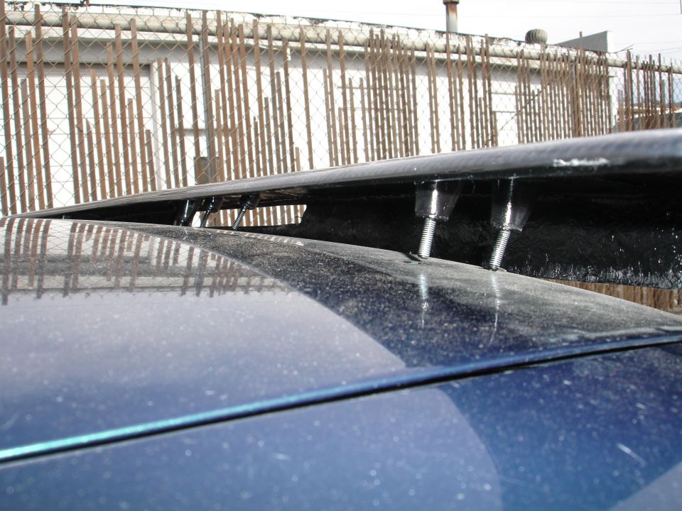 Carbon fiber spoiler bolted to a blue car's trunk lid