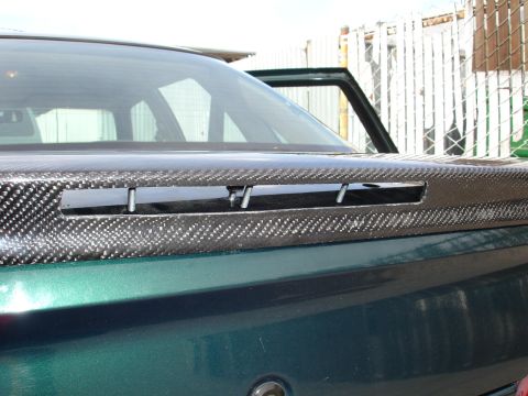 1995 Ford Taurus - Close-up of a carbon fiber spoiler mounted on the rear of a green vehicle, showing the attachment hardware.