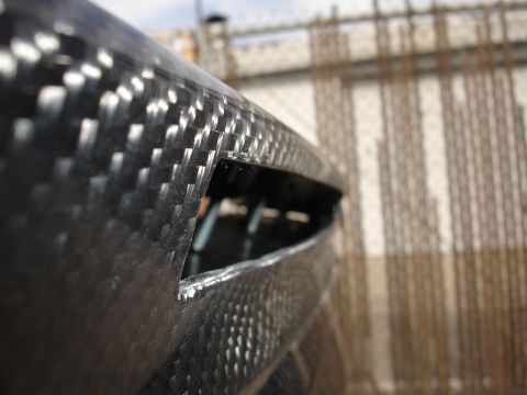 1995 Ford Taurus - Carbon fiber part with an opening, background shows construction materials.