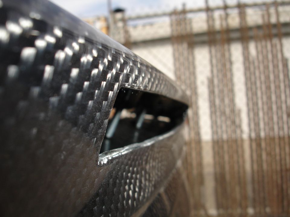 Close-up of a carbon fiber part with a cut-out opening, showing the weave pattern