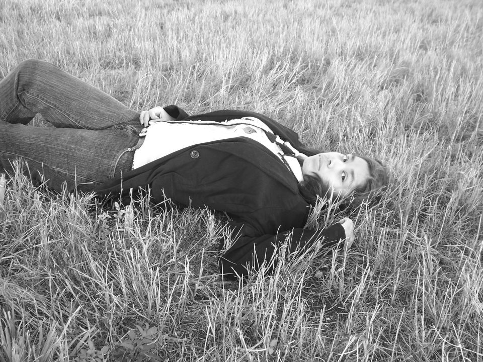 Person in jeans and jacket lying on their back in tall grass