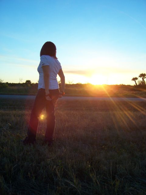 1994 Ford Probe - A woman stands in a field, silhouetted against a vibrant sunset, with palm trees in the distance.