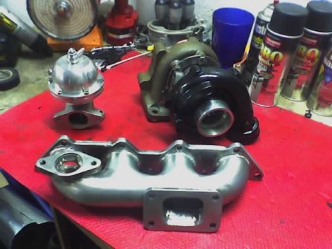 1999 Mitsubishi Mirage - A turbocharger, wastegate, and exhaust manifold are laid out on a red surface, possibly in a workshop.