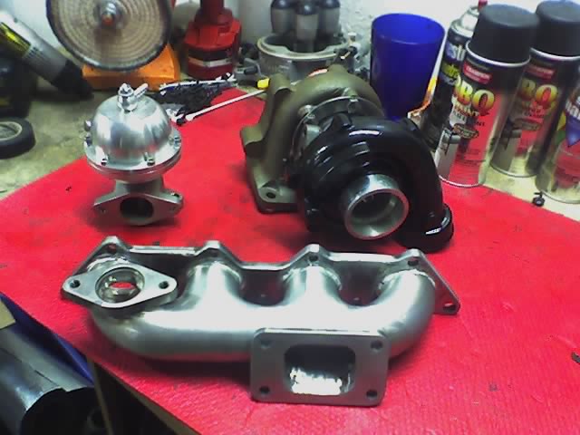 Turbo manifold, external wastegate and turbocharger laid out on a red workbench