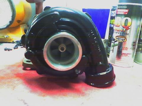 1999 Mitsubishi Mirage - A turbocharger sits on a red-stained surface next to cans of spray paint.