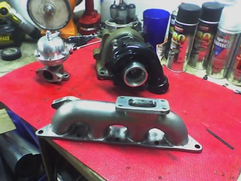 1999 Mitsubishi Mirage - Aftermarket turbocharger and wastegate components are laid out on a red surface.