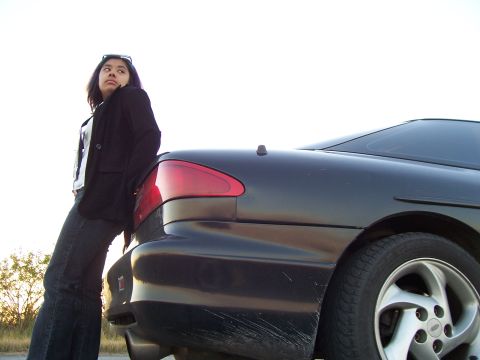 1994 Ford Probe - A woman leans against the rear of a black car, with visible scratches on the bumper.