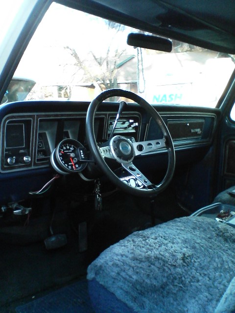1978 Ford Bronco - The interior of a vehicle shows a custom steering wheel and an added tachometer gauge.