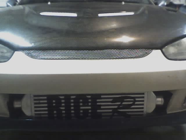 Front of tan car with carbon-fiber hood and front-mount intercooler lettered RICE in the bumper opening
