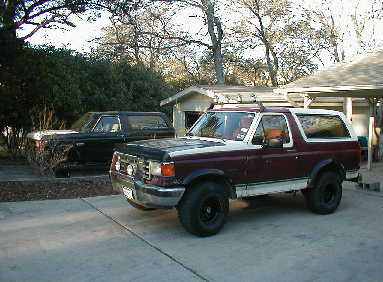 1989 Ford Bronco - A maroon and white Ford Bronco is parked in a driveway next to another vehicle.