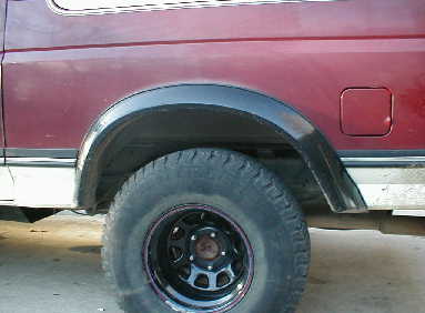 1989 Ford Bronco - Close-up of a black fender flare over a tire on a maroon vehicle, with a SuperMotors watermark.