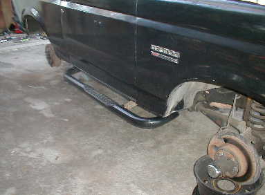 1989 Ford Bronco - Close-up of side steps and rear wheel well of a dark-colored truck.