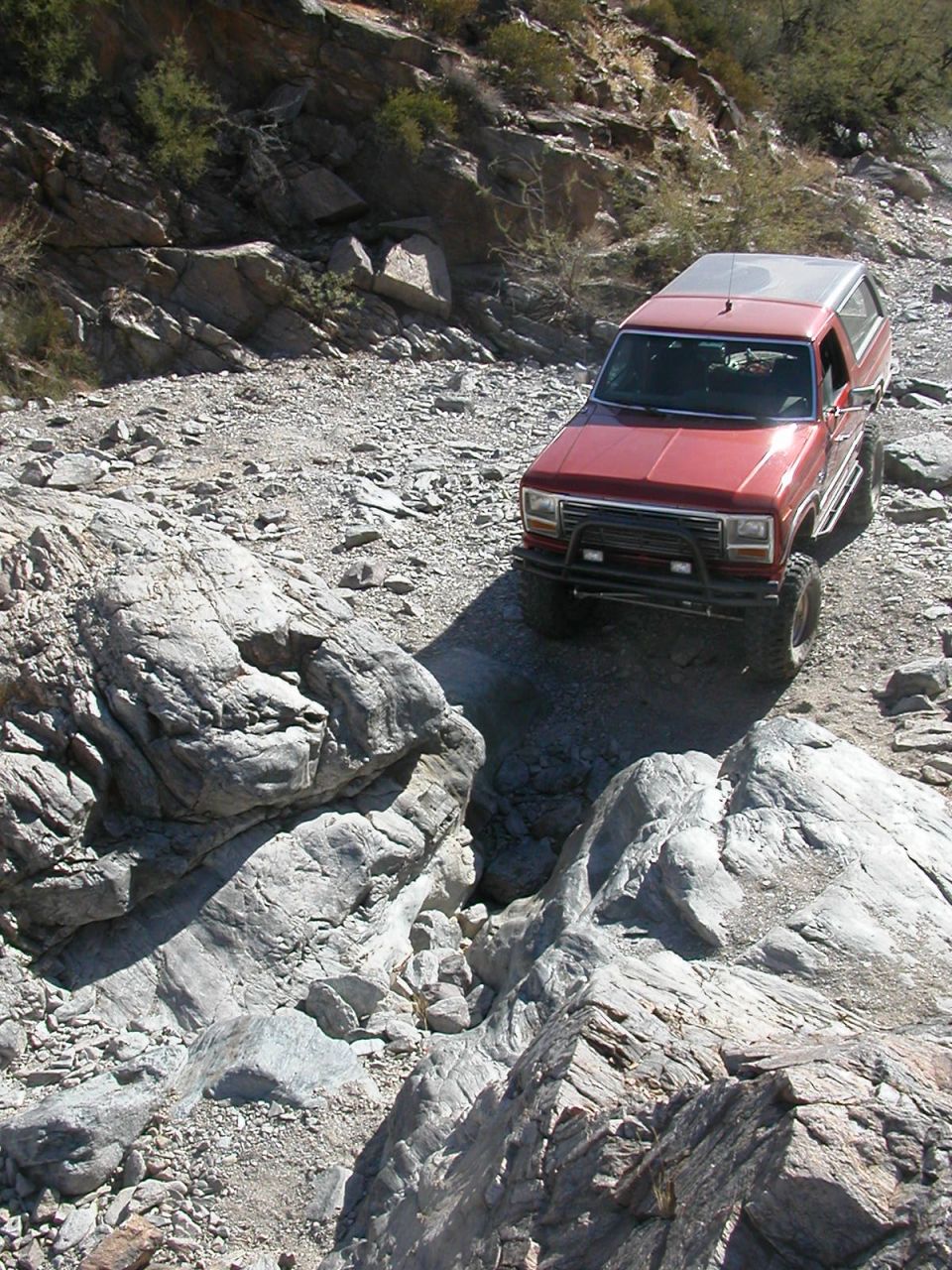 Red SUV navigating a rocky, off-road trail. It has a brush guard and lifted suspension
