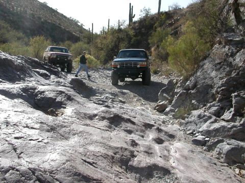1984 Ford Bronco - Two Ford Broncos navigate a challenging rocky terrain in a desert landscape.