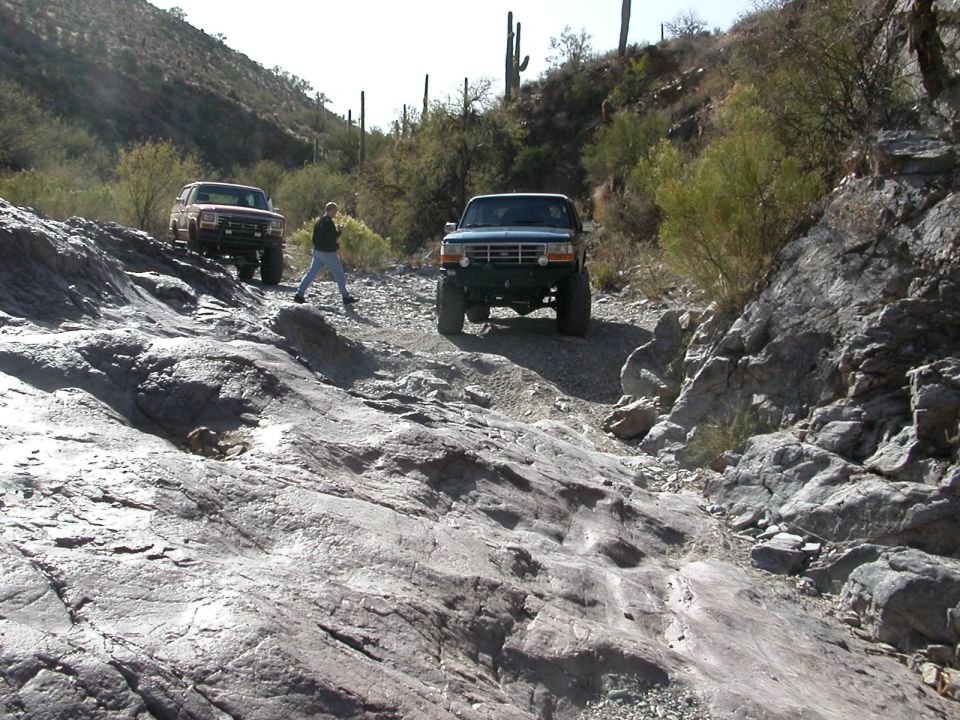 Dark green 1992 Ford Bronco driving on a rocky, desert trail