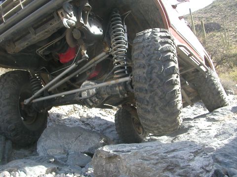 1984 Ford Bronco - Close-up of the front suspension and chassis of a 1984 Ford Bronco navigating rocky terrain.